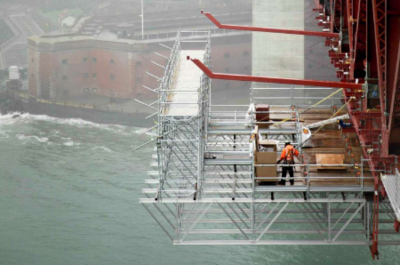 A construction worker stands on scaffolding while working to install large struts used as part of a planned suicide net sit underneath the east side of the Golden Gate Bridge in San Francisco, Calif. Wednesday, Dec. 11, 2019.