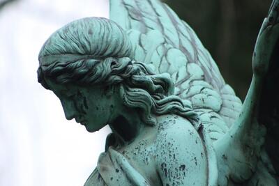 A close-up side photo of an oxidized (green) statue of an angel
