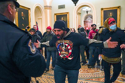 A right-wing militant in a QAnon sweatshirt gestures to a police officer after breaking into the U.S. Capitol and forcing a halt to Congress’ election certification process. (Photo by Manuel Balce Ceneta/Associated Press)